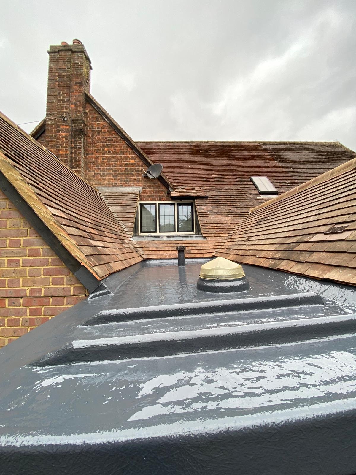 Fibreglass roofing: waterproofed flat roof with rooflight and pipe penetration between pitched tiled roofs